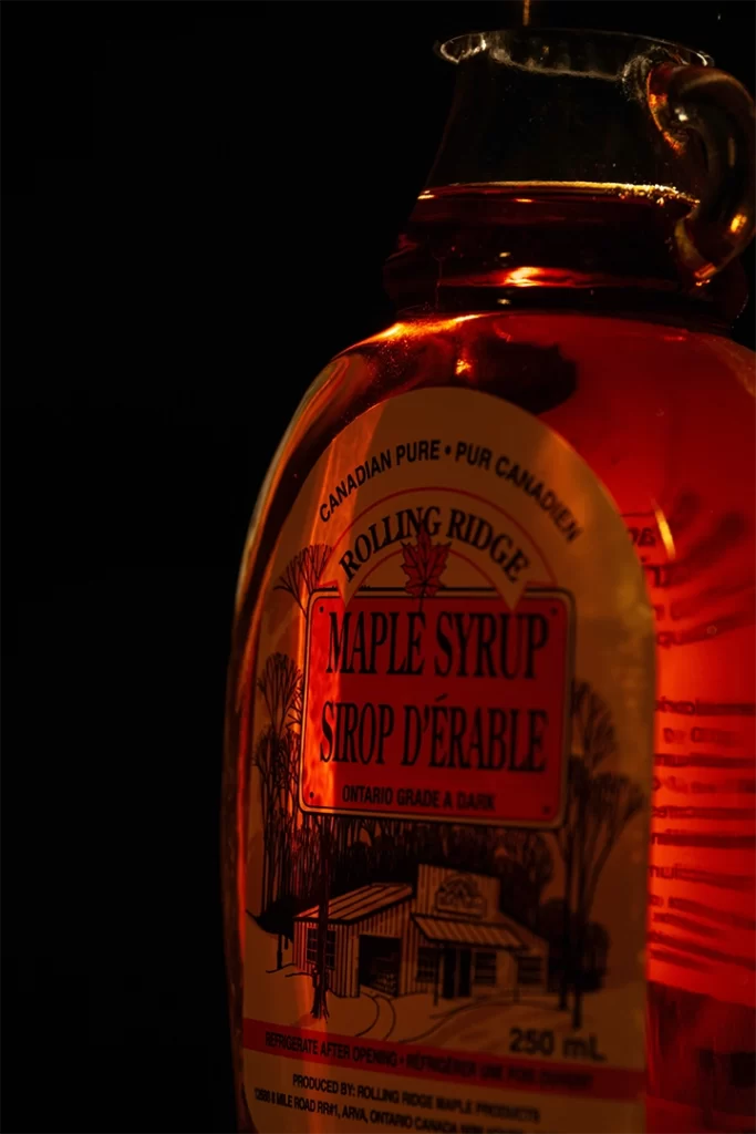 Close-up of a glass bottle of Rolling Ridge maple syrup glowing in warm light, labeled as Ontario Grade A Dark with a rustic cabin illustration. This rich, natural sweetener is a key ingredient in maple syrup coffee, known for adding depth of flavor along with potential health benefits like antioxidants and lower glycemic impact.